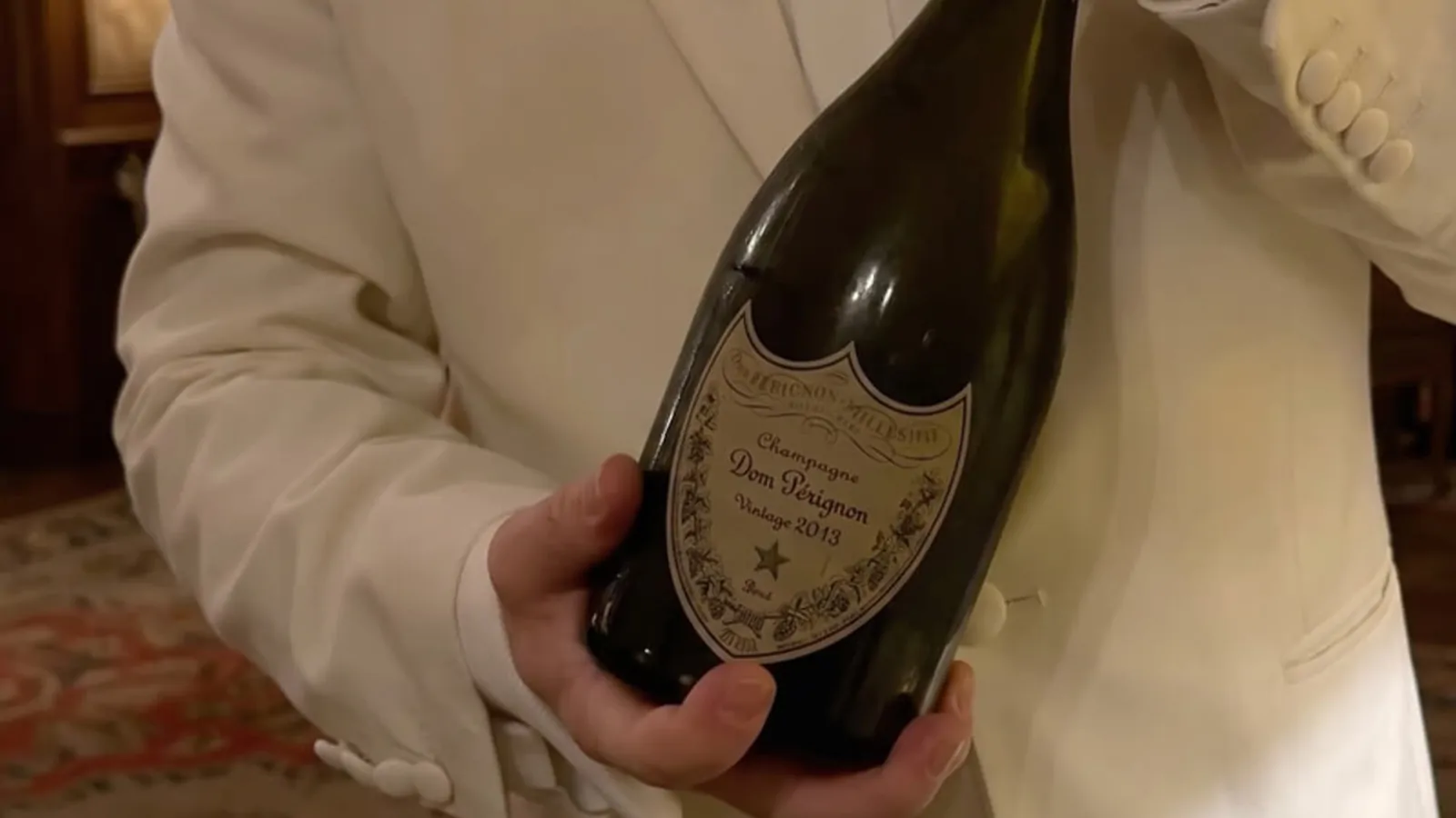 A white-jacketed server holding a bottle of Dom Pérignon Vintage 2013 champagne